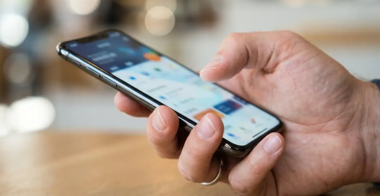 Une main tenant un smartphone avec une application bancaire moderne, l'écran est complètement flouté, sur une surface de bureau contemporaine propre